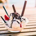 Sorvete caseiro de baunilha com calda de chocolate e pedaços de morango, decorado com chantilly e raspas de chocolate.