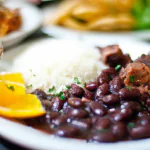 Feijoada servida em um prato branco com arroz, couve e laranja.