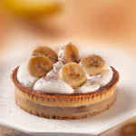 Banoffee pie em uma mesa de madeira com uma fatia cortada