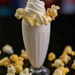Milkshake de pipoca em um copo alto com canudo, coberto com chantilly e pipoca