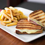 Misto quente grelhado em um prato branco, com uma porção de batatas fritas ao lado.